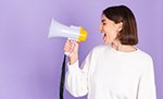 Young brunette in white casual sweater isolated on purple background happy screaming in megaphone copy space point left